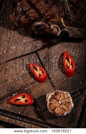 Tasty dinner. Top view of fresh pepper with garlic and tasty juicy steak lying on a wooden table while being cooked in a restaurant kitchen.