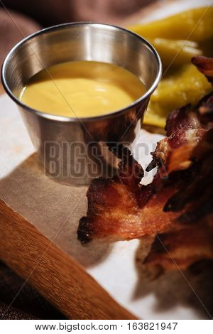 Spicy meal. Close up of fried bacon and sauce standing on wooden tray after being cooked in a restaurant.