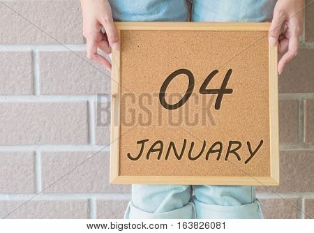 Closeup calendar at the cork board in hand of asian woman in front of her legs with 4 january word on brick wall textured background