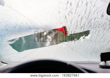 Woman Deicing Front Car Windshield With Scraper