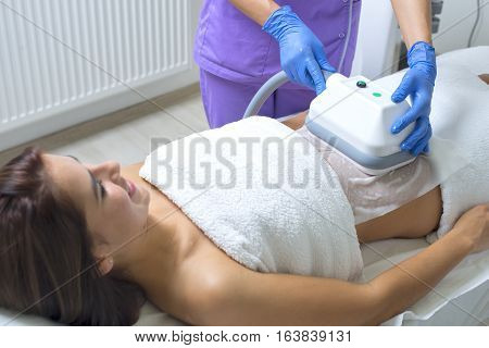 Pretty young woman getting cryolipolyse treatment in cosmetic cabinet
