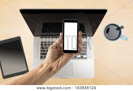 Male hand holding a smartphone with a blank screen over organized desk with laptop blurred in background with copy space