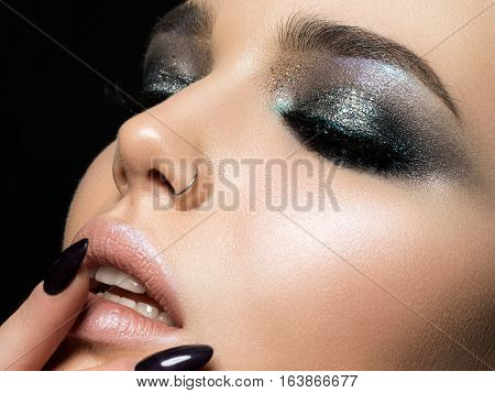 Close up view of beautiful woman touching her lips. Perfect skin and evening makeup. Macro studio shot. Sensuality passion cosmetology lip care plastic surgery or injection concept.