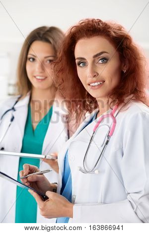 Portrait of two female doctors standing with clipboard and tablet ready to work. Health care medical service or education and teamwork concept.