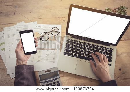 Business woman hand holding smartphone and using laptop computer and calculator for analyzing stock maket in office. vintage effect.