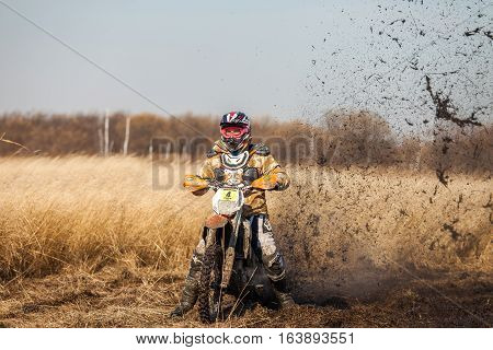 KHABAROVSK RUSSIA - OCTOBER 23 2016: Enduro bike rider on a field with dry grass in autumn. The motorcycle skids and makes a lot of mud splashes