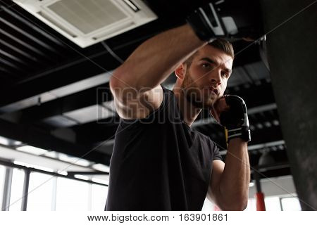 Young man exercising boxing in black gloves in gym