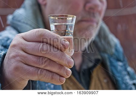 Man holding a shot of heavy drink standing outdoor under a showering snow. Closeup cropped shot
