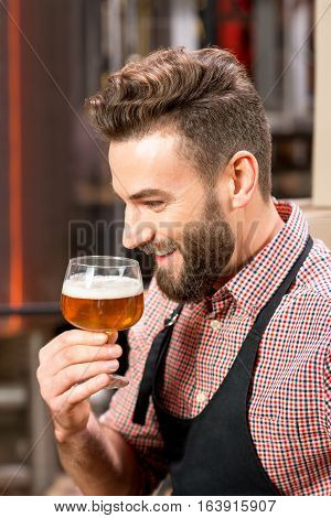 Handsome brewer expertising beer in the glass at the manufacturing