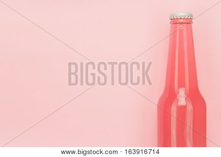 glass bottle of pinkish soda drink on pink background