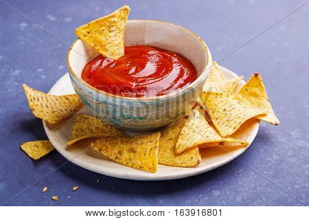 Nachos on plate and red sauce on a blue background. Shallow DOF