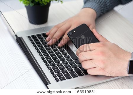 Alushta Russia - November 2 2016: Man hand with Apple Watch holding iPhone 7 Jet Black over Macbook Pro. iPhone 7 was created and developed by the Apple inc.