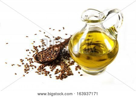 Brown flax seeds on a spoon and linseed oil in a glass jug isolated on a white background