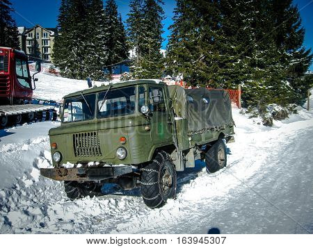 Freight car snowmobile with chains on the wheels on the snow-covered road with trees