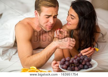 Couple eating fruits in bed. Young woman and man indoor. How does it taste.