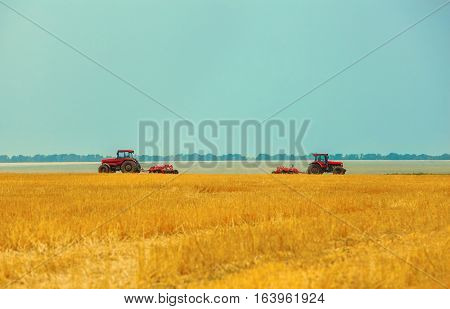 Summer day two tractors to plow plow the soil on sloping wheat. Agricultural land treatment before planting.