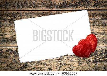 Two red hearts and a sheet of paper on wooden texture