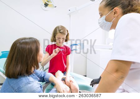 Mother And Little Daughter Visiting Dentist At Dental Clinics. Orthodontist Puts On, Corrects The De