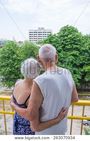 Senior Couple Standing Oustide At Balccony At Home And Looking Awayat Green Trees