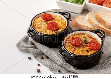 Slovak Christmas Cabbage Soup In Two Small Pots With Sausage On Top On White Background.