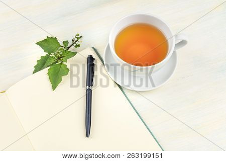 A Photo Of An Open Journal With A Branch With Green Leaves, A Pen And A Cup Of Tea, With Copy Space