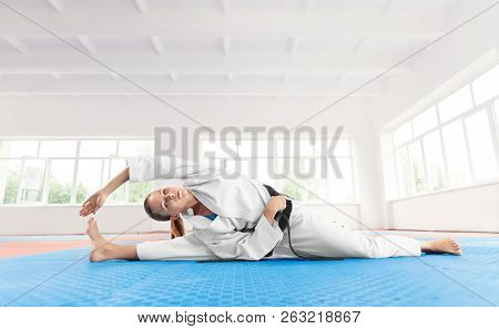 Young Active Girl Wearing In White Kimono With Black Belt, Doing Exercise On Flexibility. Seriously 