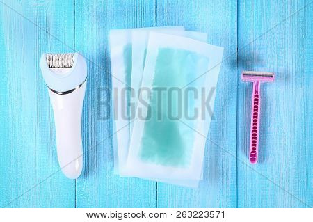Means For Hair Removal. Epilator, Razor For Shaving, Wax Strips On A Tropical Leaf On A Blue Wooden 