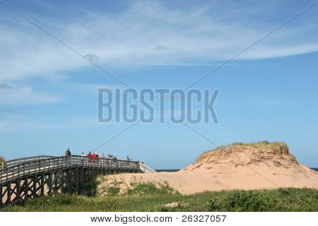 Lidí, kteří jdou po promenádě prostřednictvím písečnými dunami na pláži v národním parku Cavendish, Pr