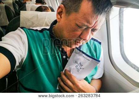 Suffering Asian Man Holding Air Sickness Vomit Bag In Airplane
