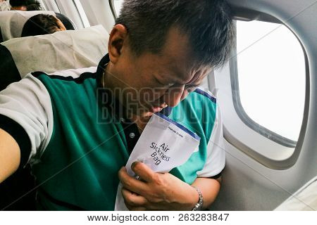 Suffering Asian Man Holding Air Sickness Vomit Bag In Airplane