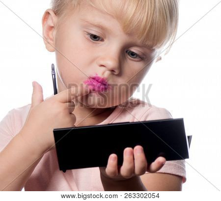 attractive young caucasian little girl doing makeup applying l?pst?k looking in the mirrow studio shot isolated on white