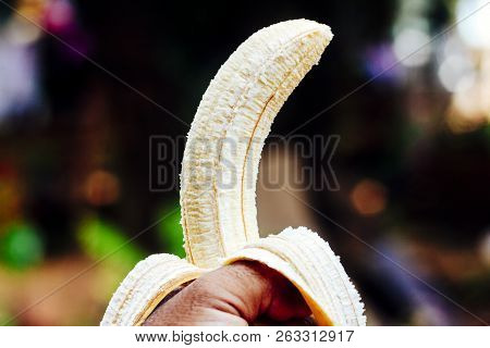 Person Holding A Peeled Banana On A Blurred Background