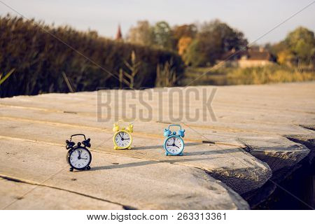 Three Small Alarm Retro Clocks On Wooden Surface. Autumn Abstract Photo.