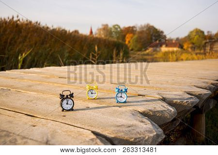 Three Small Alarm Retro Clocks On Wooden Surface. Autumn Abstract Photo.