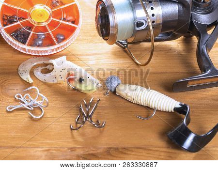 Spinning Reel, Spoon-bait, Wobblers, Hooks And Small Round Boxes On A Wooden Background