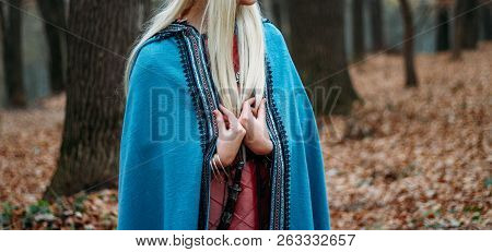 A Girl With Long Hair, Blonde, In A Blue Cape And A Pink Dress, Walks Through The Autumn Forest, Alo