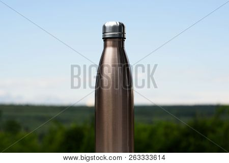 Thermo Stainless Bottle For Water, Tea Or Coffee. Sky And Forest On Background. On The Glass Desk. T