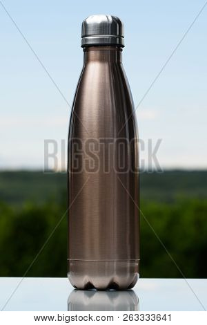 Thermo Stainless Bottle For Water, Tea Or Coffee. Sky And Forest On Background. On The Glass Desk. T