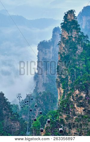 Famous tourist attraction of China - Zhangjiajie stone pillars cliff mountains in fog clouds with cable railway car lift at Wulingyuan, Hunan, China. With camera pan