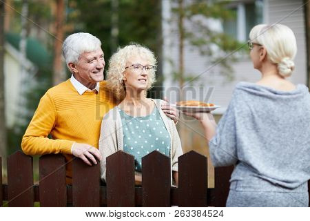 Mature woman giving her new neighbours homemade fresh apple pie on plate over fence
