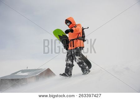 Man Walking With The Snowboard In Hands Down The Hill In The Mountain In The Popular Tourist Resort 