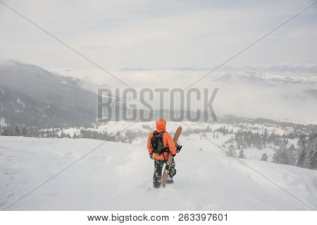 Rear View Man Standing With The Snowboard In The Mountains And Looking Into A Distance In The Popula