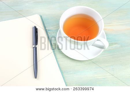 A Photo Of An Open Journal With A Pen And A Cup Of Tea, Shot On A Teal Blue Background