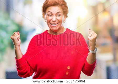 Atrractive senior caucasian redhead woman wearing winter sweater over isolated background celebrating surprised and amazed for success with arms raised and open eyes. Winner concept.