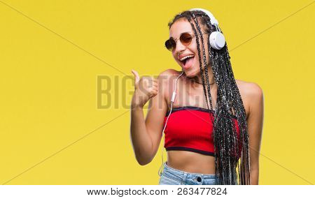 Young braided hair african american with birth mark wearing headphones over isolated background doing happy thumbs up gesture with hand. Approving expression looking at the camera