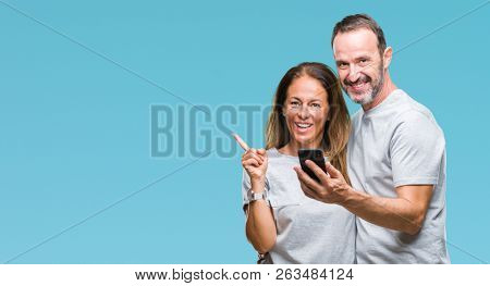 Middle age hispanic couple texting message on smartphone ver isolated background very happy pointing with hand and finger to the side