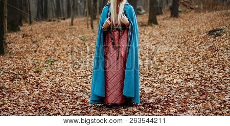 A Girl With Long Hair, Blonde, In A Blue Cape And A Pink Dress, Walks Through The Autumn Forest, Alo