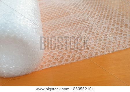 Transparent Bubble Wrap Roll For Packaging Fragile Items On Brown Wooden Table, Front View