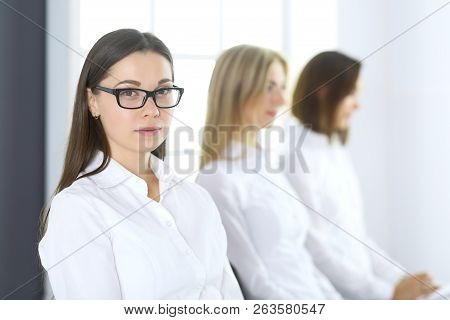 Attractive Businesswoman At Meeting Or Conference Against The Background Of Colleagues. Group Of Bus