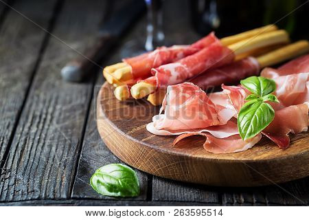 Bread Sticks Grissini With Prosciutto Ham On Cutting Board Over Wooden Background, Close Up